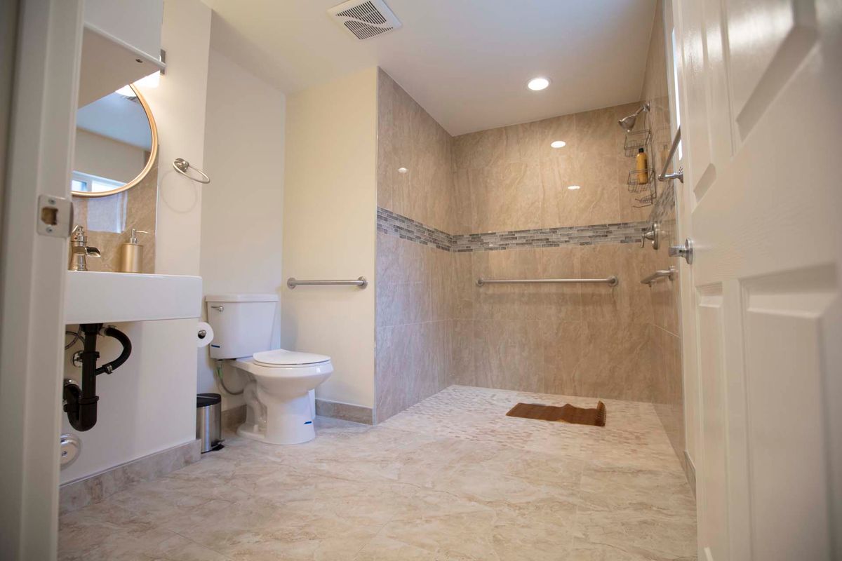 A spacious, accessible bathroom featuring a walk-in shower with grab bars and modern design elements.