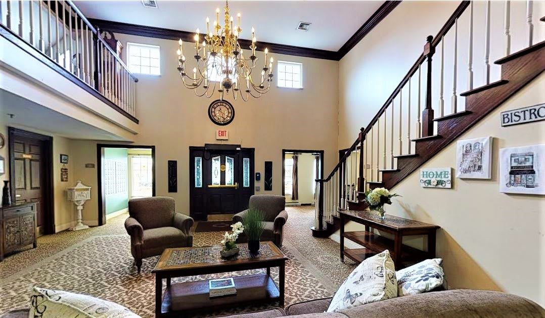 A spacious living room with elegant decor, featuring a chandelier, comfortable seating, and a staircase leading to the upper floor.