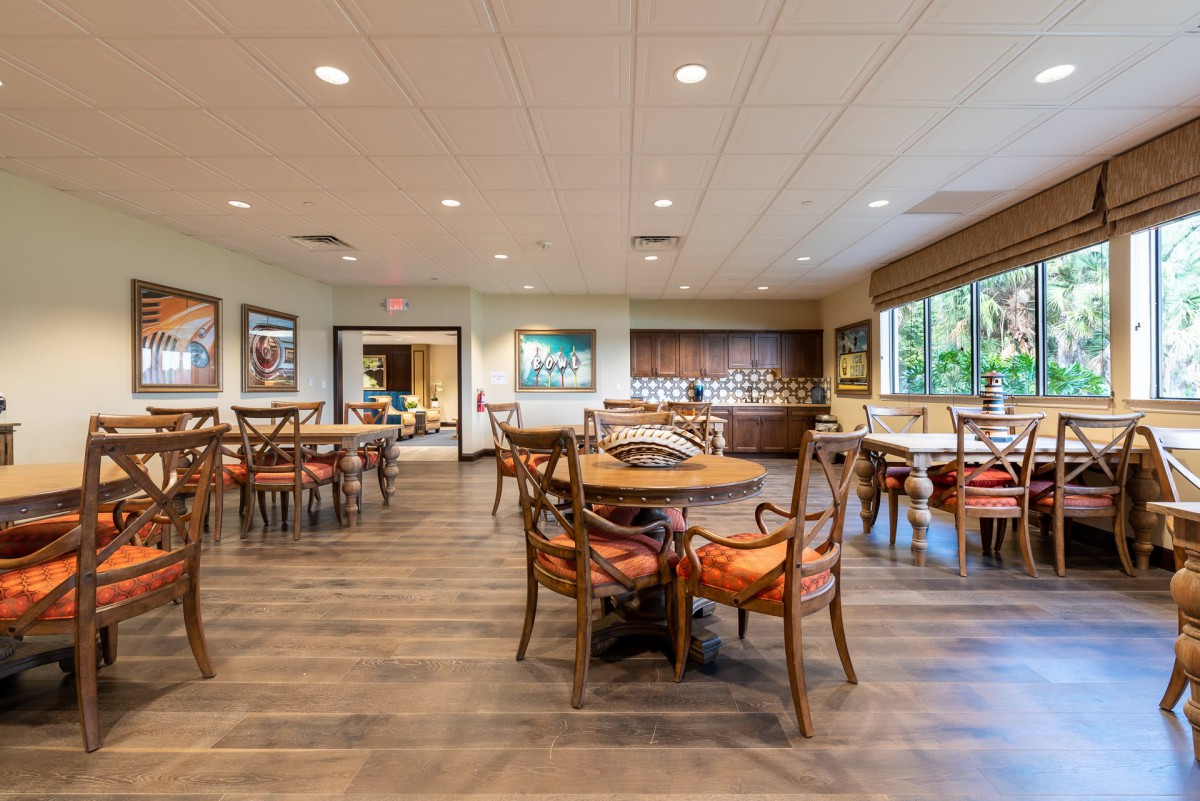 An indoor dining area with wooden flooring, tables and chairs, ceiling lights, and large windows.