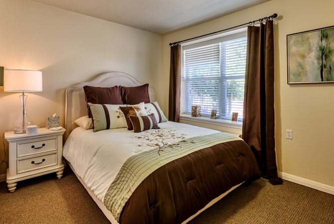 A cozy bedroom featuring a neatly made bed with brown and white bedding, flanked by a large window with curtains.