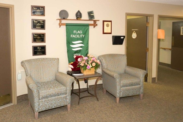 A comfortable office waiting area with chairs, a table with flowers, and several awards displayed on the wall.