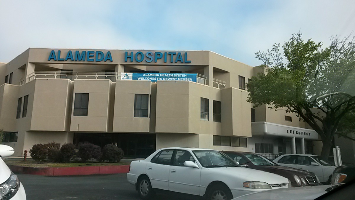 A hospital building with a visible parking lot and a car in the foreground.