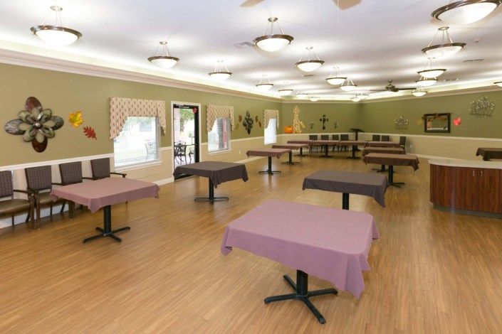 An empty dining area with tables covered in purple tablecloths and a wooden floor.