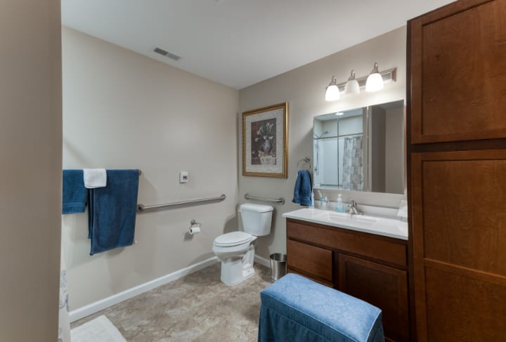 A well-lit bathroom with accessible features, including a grab bar by the toilet and blue towels accenting the decor.