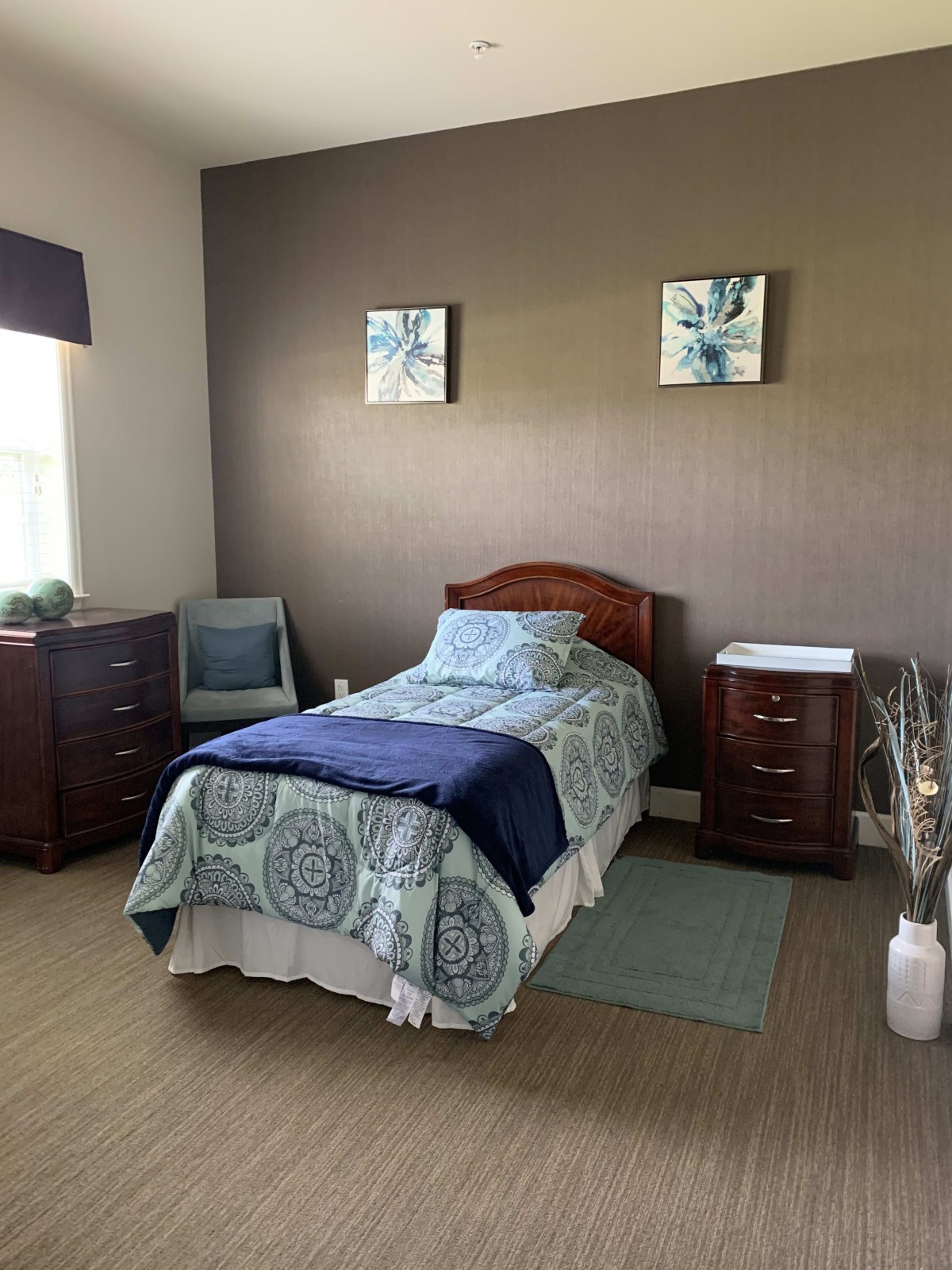 A cozy bedroom with a single bed, two dressers, and an armchair.