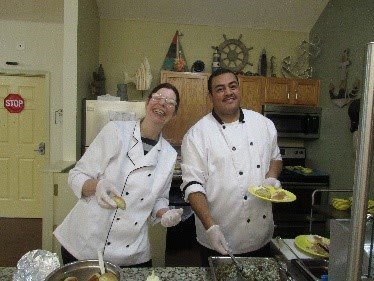 Two chefs smiling in a kitchen while preparing food.