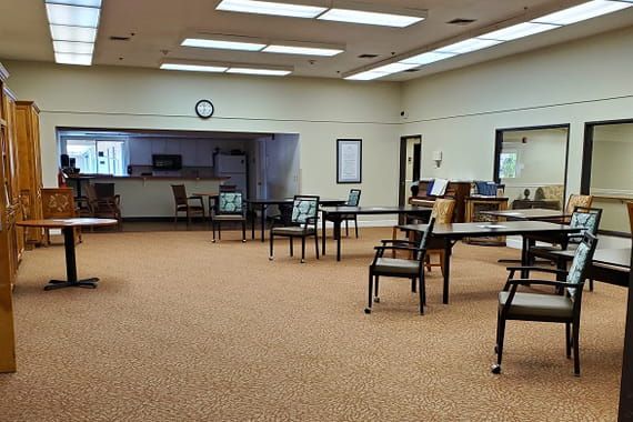 An empty waiting room with chairs and tables arranged on a carpeted floor.