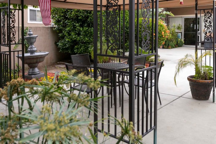 A cozy patio setup featuring a table and chairs under an umbrella, surrounded by plants.