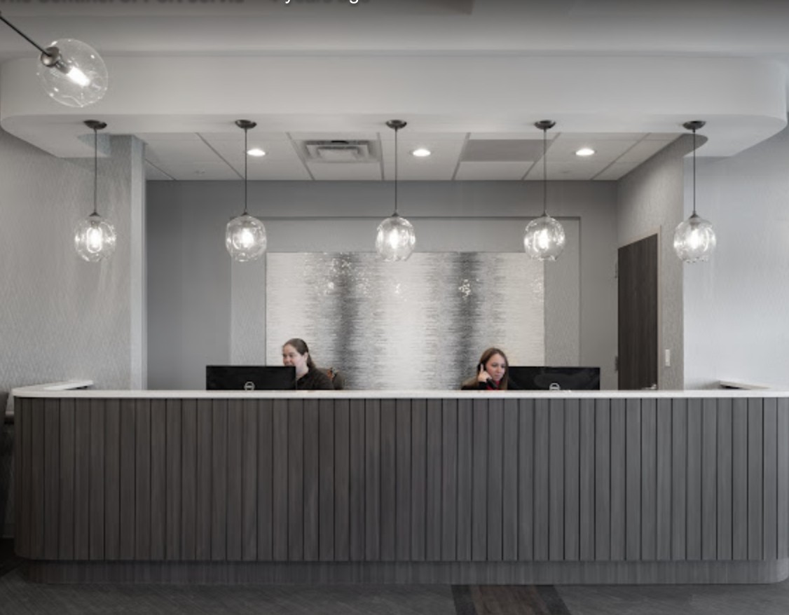 A modern office reception area with two staff members at the desk and stylish pendant lighting.