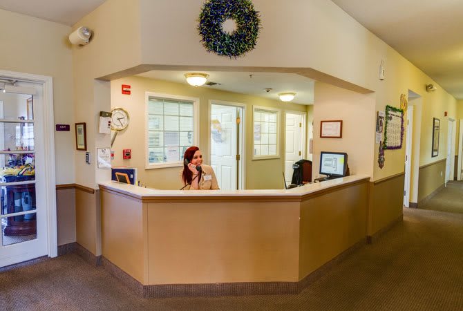 A woman at a reception desk in an office setting, speaking on the phone.