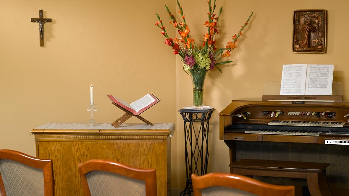 A serene room with a book on a stand, vibrant flowers in a vase, and an organ.