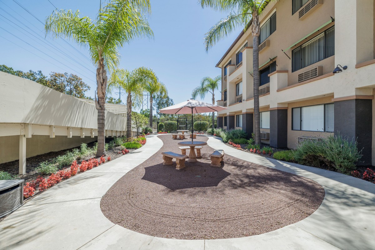 A sunny outdoor patio area with seating and landscaping beside an apartment building.