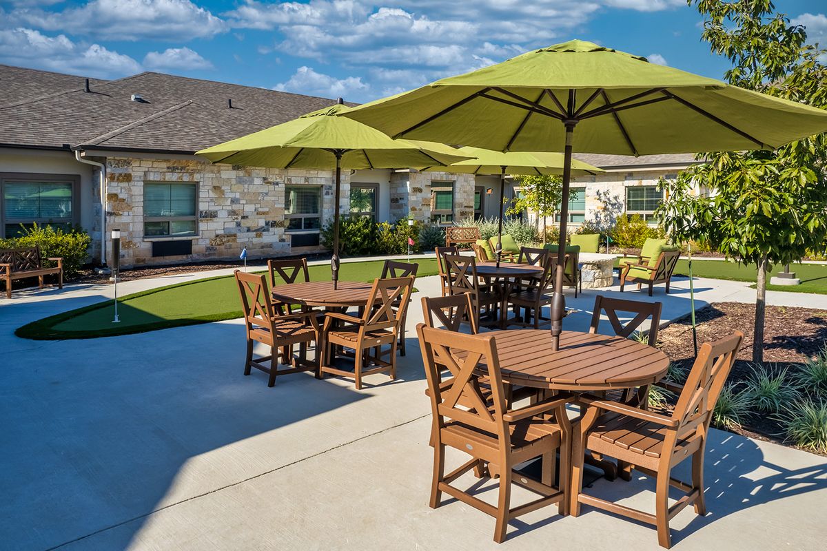 Outdoor patio area with tables, chairs, and umbrellas in a landscaped setting.