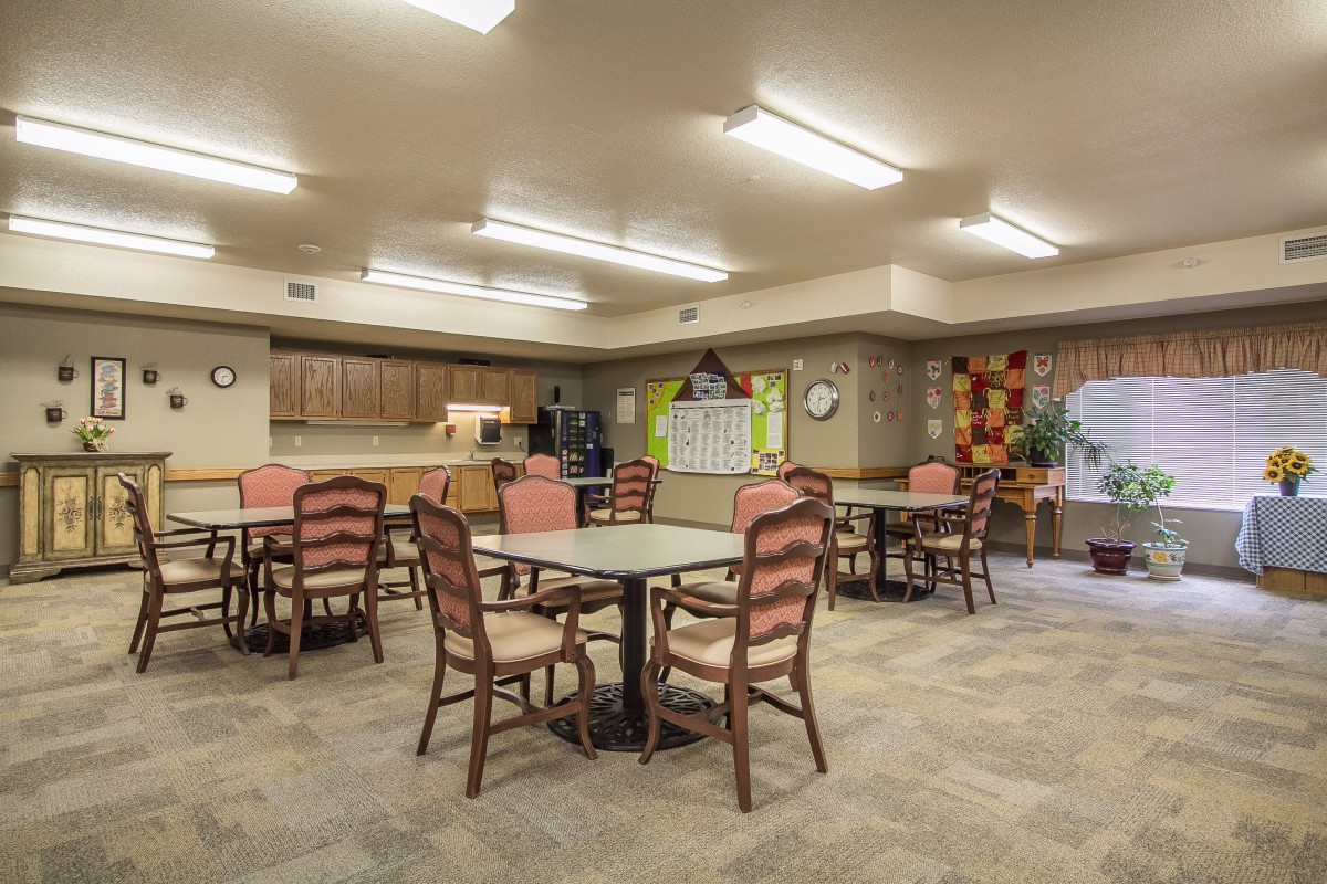 A spacious community dining room with tables and chairs, adjacent to a kitchen area.