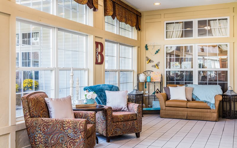 A cozy living room features armchairs and a sofa, with large windows allowing natural light to flood the space.