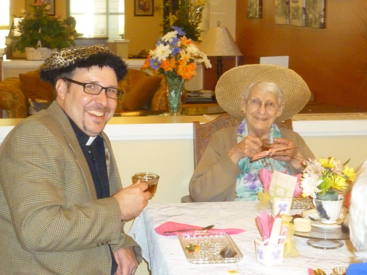 Two people enjoying a tea party, wearing hats and smiling.