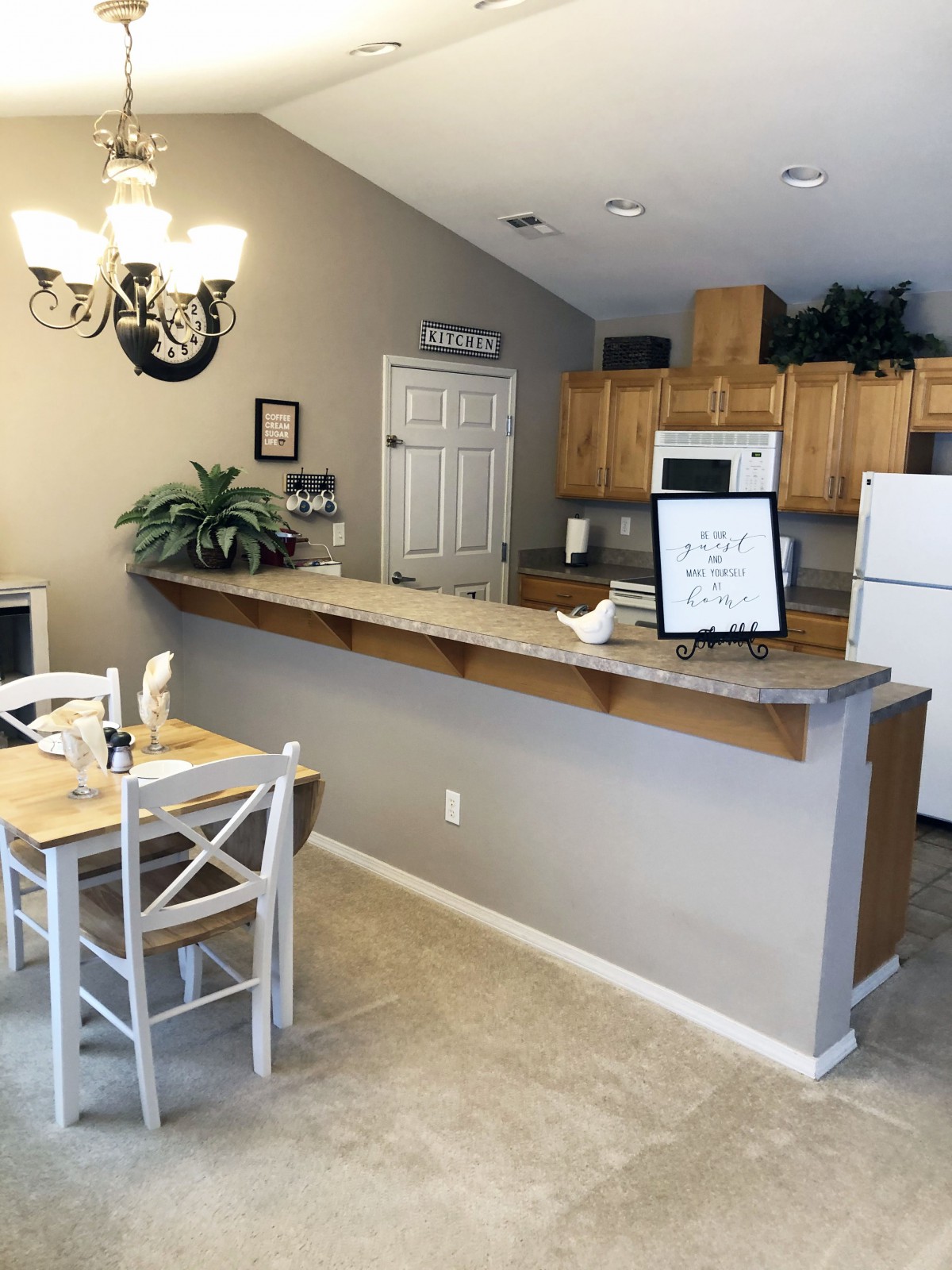 A cozy kitchen and dining area with a small table, chairs, wood cabinets, and a chandelier.