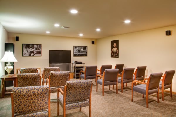 A cozy home theater room with seating arranged in rows facing a television, decorated with wall art and bright lighting.