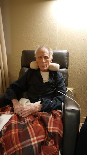 An elderly man sitting comfortably in a chair, warmly wrapped in a blanket.