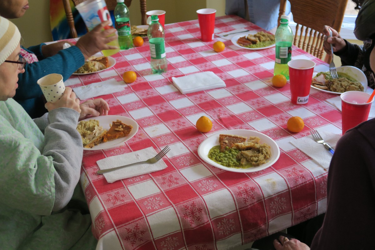 A dining table with a checkered tablecloth set for a meal, including plates of food, plastic bottles, and red cups.