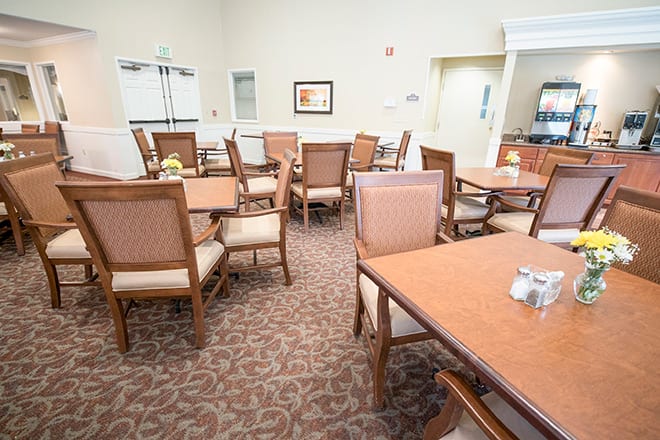 A well-lit dining area with several tables and chairs arranged on a carpeted floor.