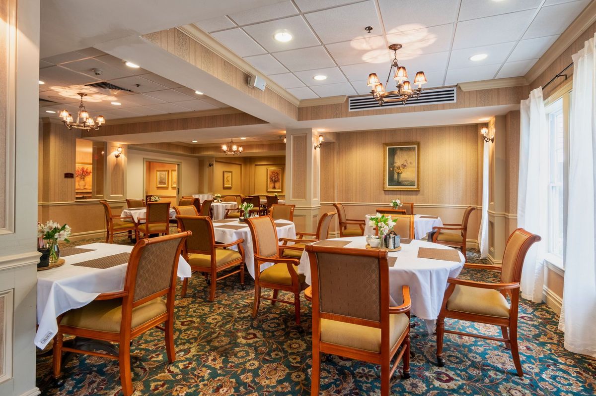 An elegant dining room with neatly arranged tables and chairs, featuring a chandelier and classic decor.