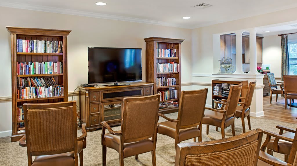 A cozy TV room with wooden chairs and bookshelves surrounding a large television.