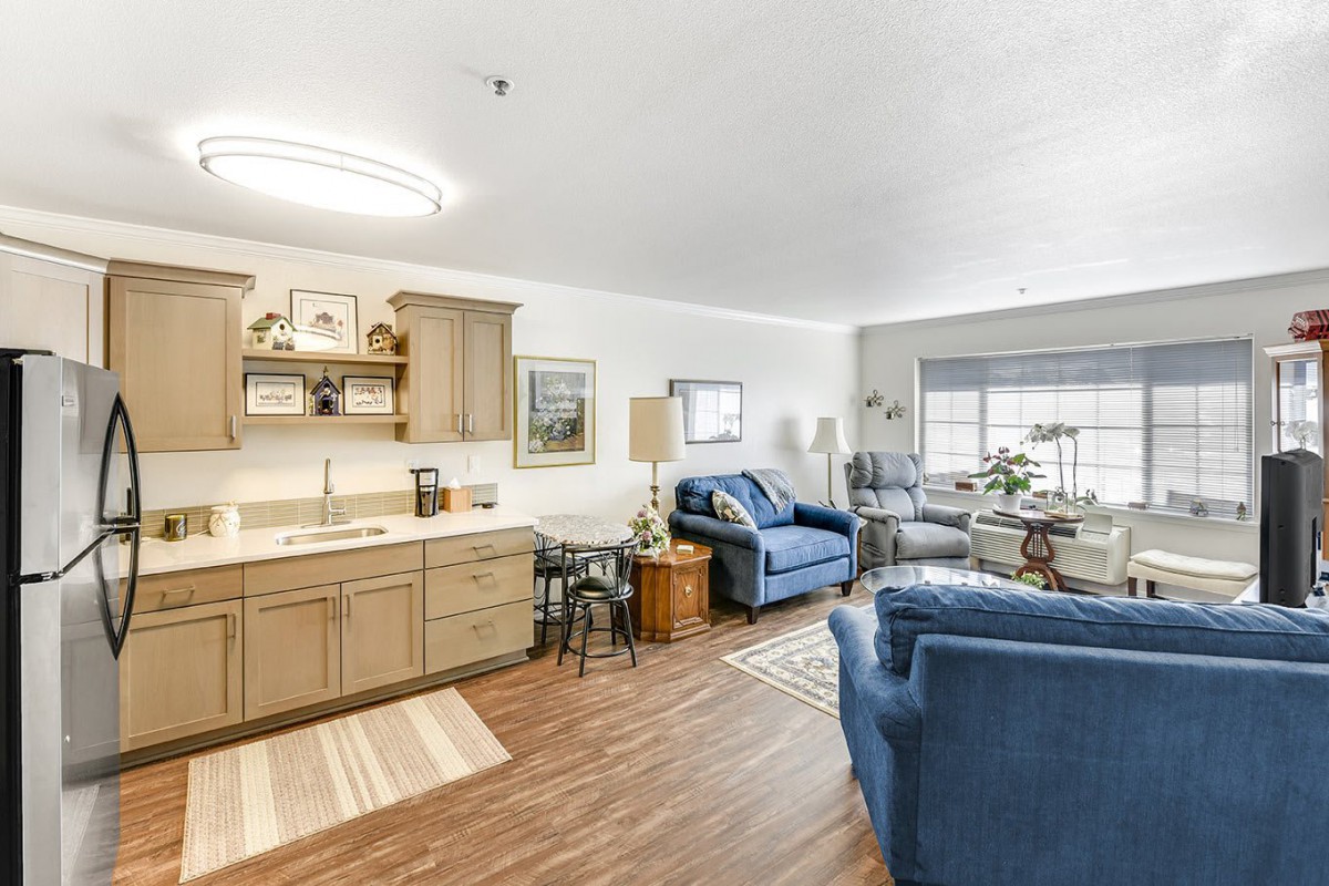A cozy open floor plan combining a modern kitchen and living room with wood flooring, featuring a blue sofa and stylish decor.