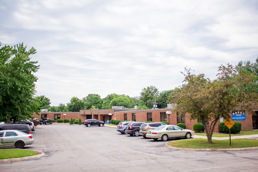 A view of a brick building with parked cars in a lot under a cloudy sky.
