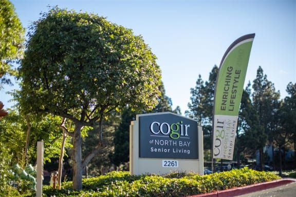 Entrance sign for COGIR of North Bay Senior Living surrounded by greenery.