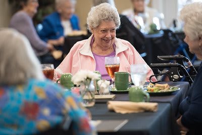 An elderly woman enjoys a meal during a social gathering.
