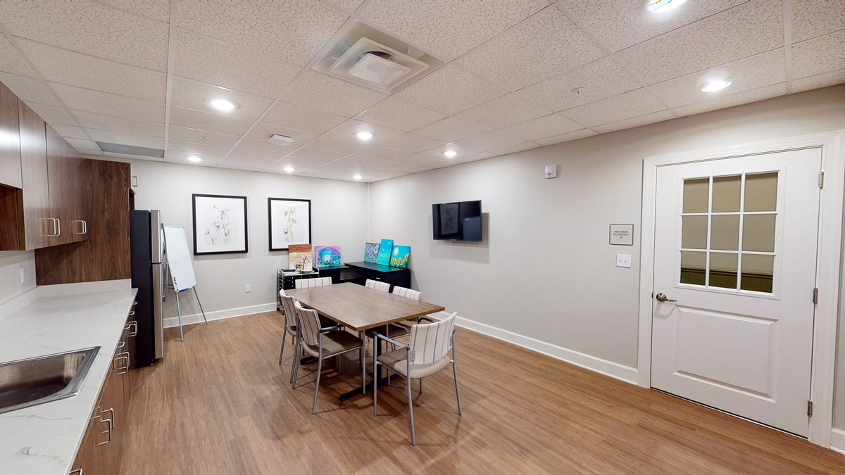 A modern meeting room equipped with a conference table, chairs, and a wall-mounted television.