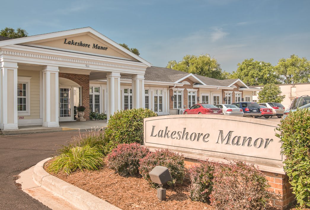 The image shows the entrance of Lakeshore Manor, featuring manicured landscaping and signage.