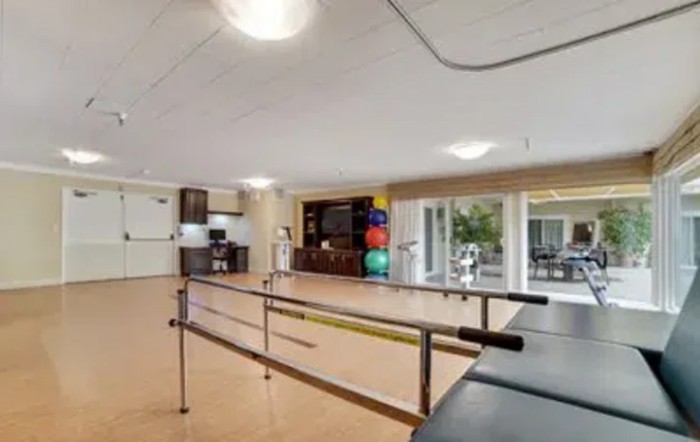 A spacious physical therapy room equipped with parallel bars and exercise balls.