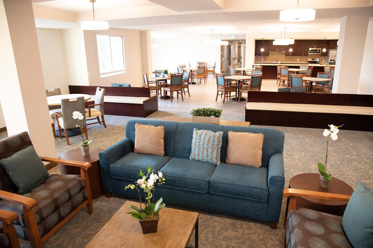 A modern living room with a blue sofa and open dining area in the background.