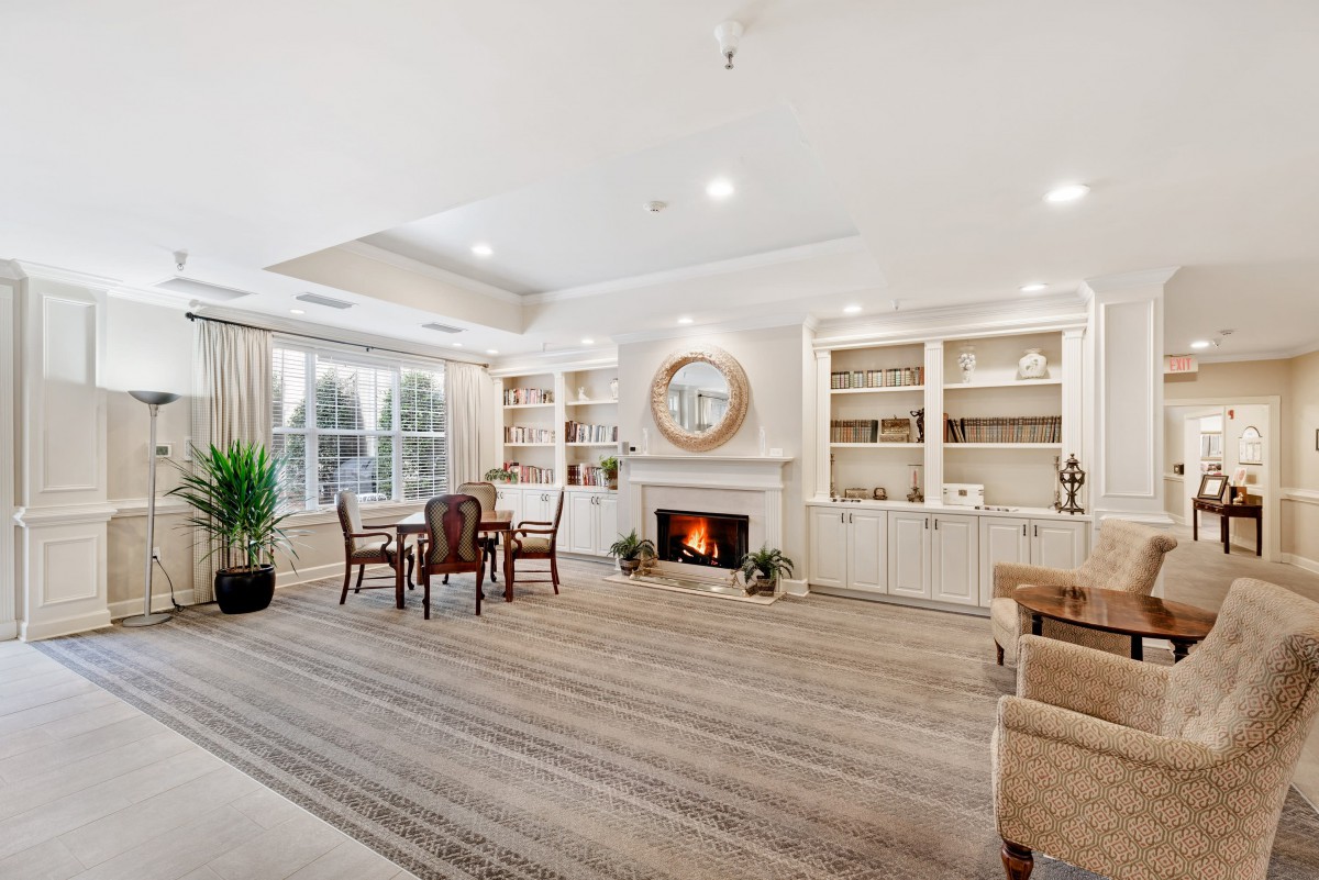 A spacious and elegantly decorated living room with a fireplace, bookshelves, and a seating area.