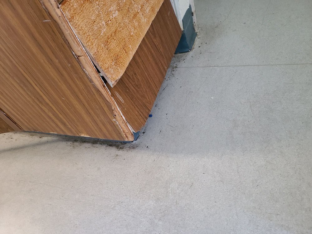 A corner of a worn and damaged wooden desk resting on a smooth floor.