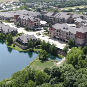 Aerial view of a residential apartment complex next to a scenic lake surrounded by trees.