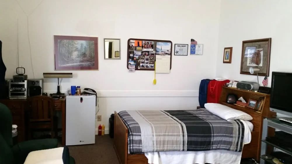 A neatly organized dorm room with a bed, bulletin board, and mini fridge.