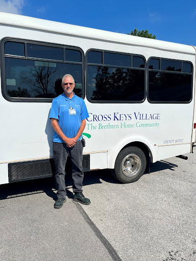 A man stands next to a community bus from Cross Keys Village, promoting local transportation services.