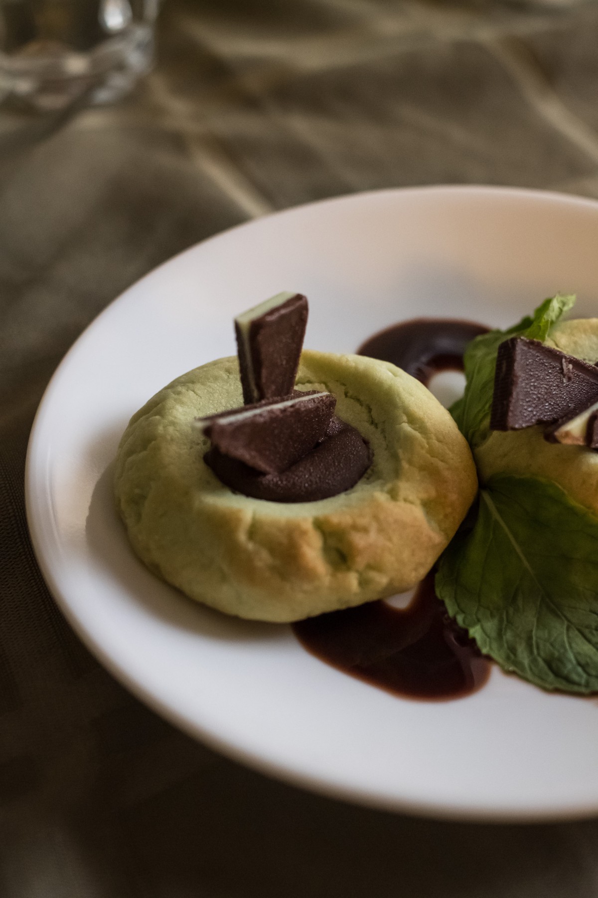 A plate featuring pastries topped with chocolate and garnished with a leaf.