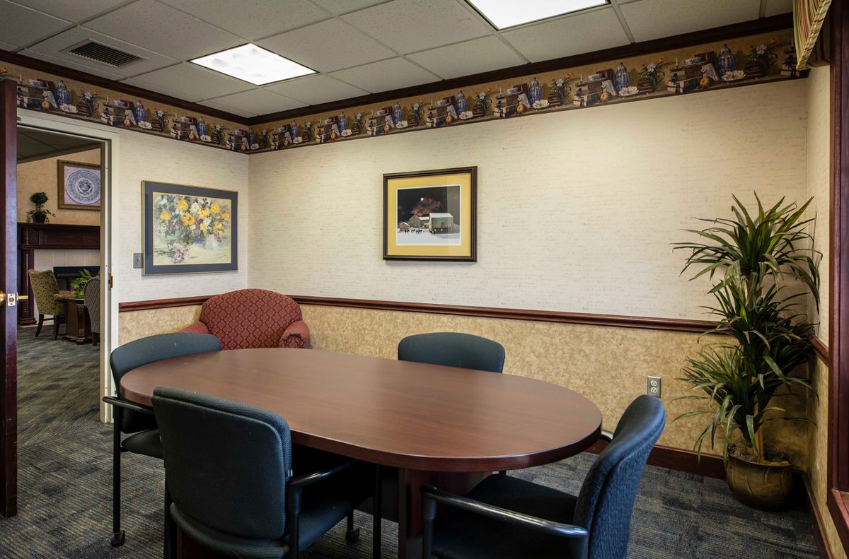 A conference room with a large oval table and several chairs, decorated with artwork on the walls.