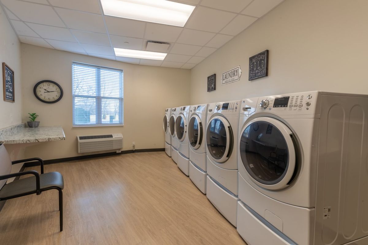 A clean and well-organized laundry room with several washing machines and dryers lined up against the wall.