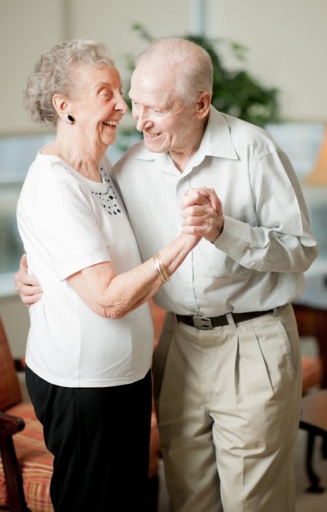 An elderly couple joyfully dancing together indoors.