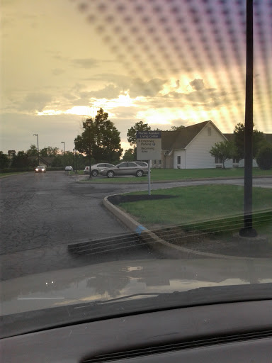 A tranquil sunset scene in an urban area, featuring a road lined with trees and parked vehicles.