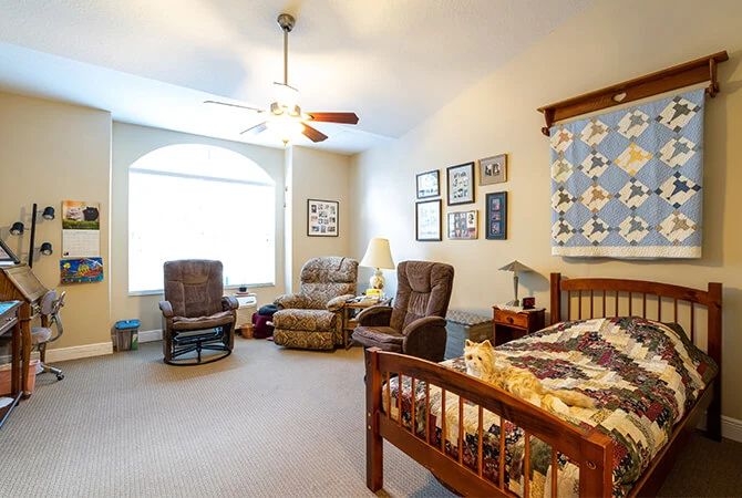 A cozy bedroom with a bed, two chairs, and various decorations on the walls.