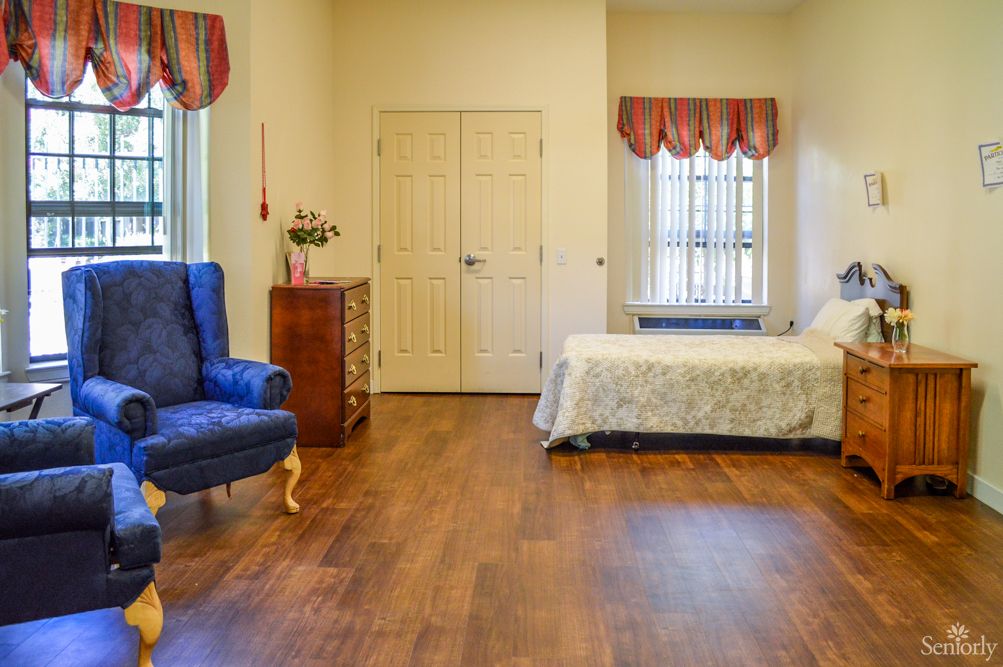 A cozy bedroom with a bed, blue armchair, dresser, and hardwood flooring.