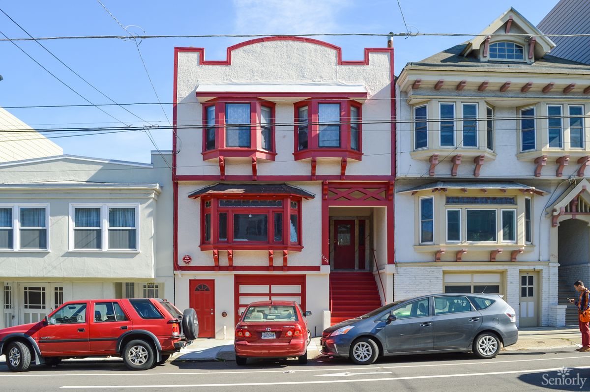 A vibrant red and white house in an urban neighborhood, flanked by parked cars along the street.