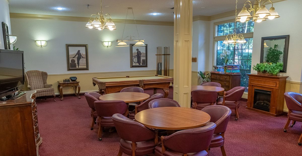A cozy lounge area with round tables, leather chairs, and a pool table under elegant chandeliers.