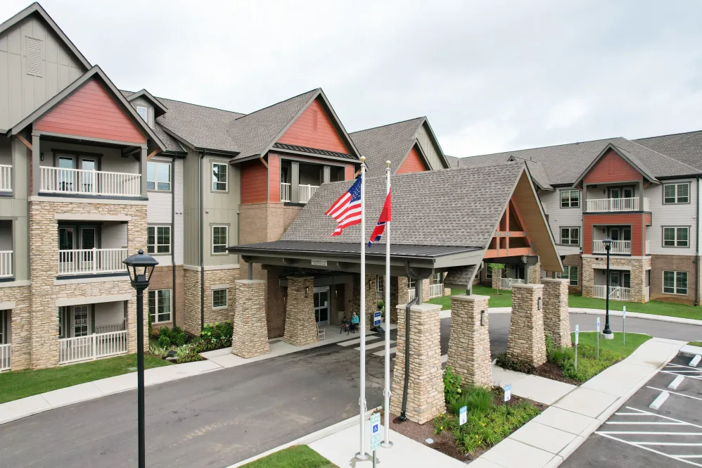 A modern residential building with an entrance featuring American and red flags, surrounded by well-maintained landscaping.
